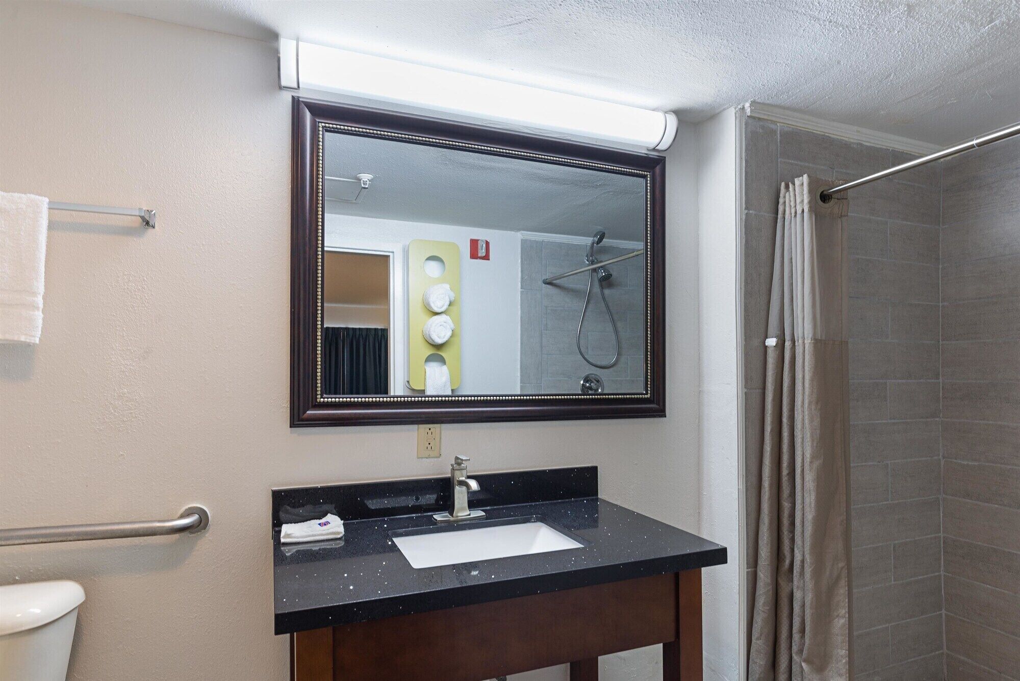 Een badkamer met een grote spiegel, een wastafel, een handdoekhouder en een douche.