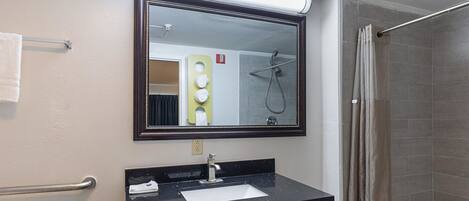Un bany amb un mirall gran, un lavabo, una barra de tovalloles i una dutxa.