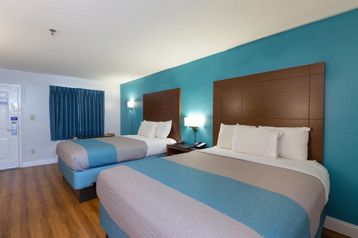 A hotel room with two beds, wooden headboards, and a blue accent wall.