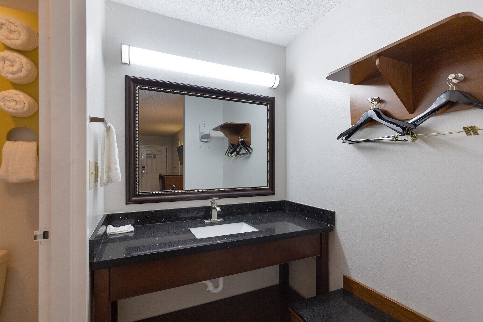 A bathroom with a black countertop sink, a large mirror, and a towel rack with towels.