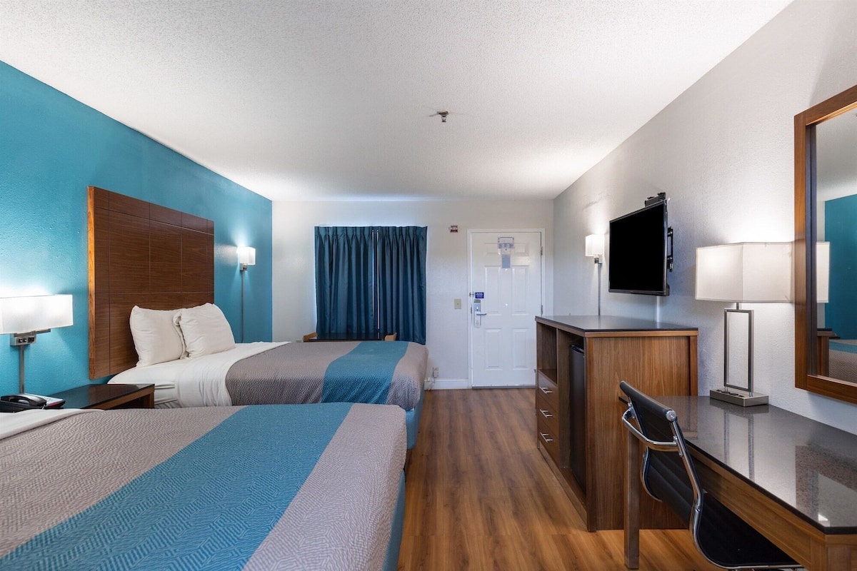 A hotel room with two beds, a desk, a TV, and a mirror.