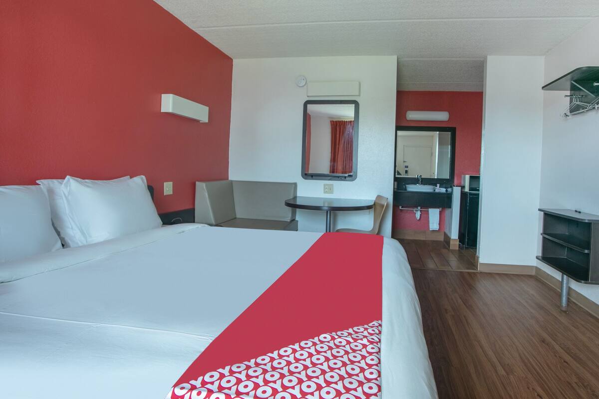 Une chambre d’hôtel avec un grand lit, une petite table, une chaise, un bureau et une salle de bain équipée d’un miroir et d’un lavabo.
