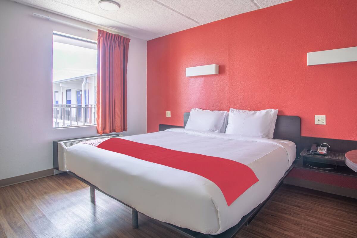 Une chambre d’hôtel avec un grand lit, un mur d’accent rouge, une fenêtre avec des rideaux et une table de chevet avec un téléphone.