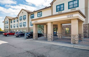A multi-story hotel with a lobby entrance, numbered 1225, and a parking lot with several SUVs.