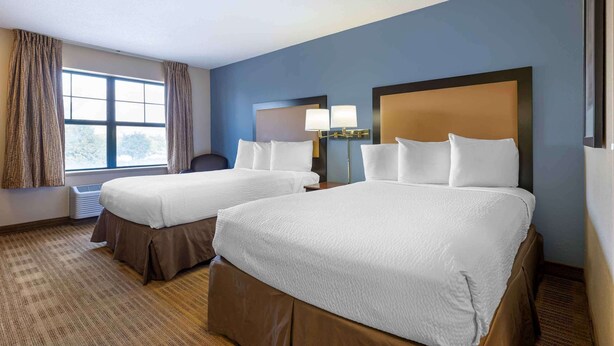 A hotel room with two beds, a large window with curtains, a desk, and a lamp. - Extended Stay America Suites Chicago Romeoville Bollingbrook (Romeoville)