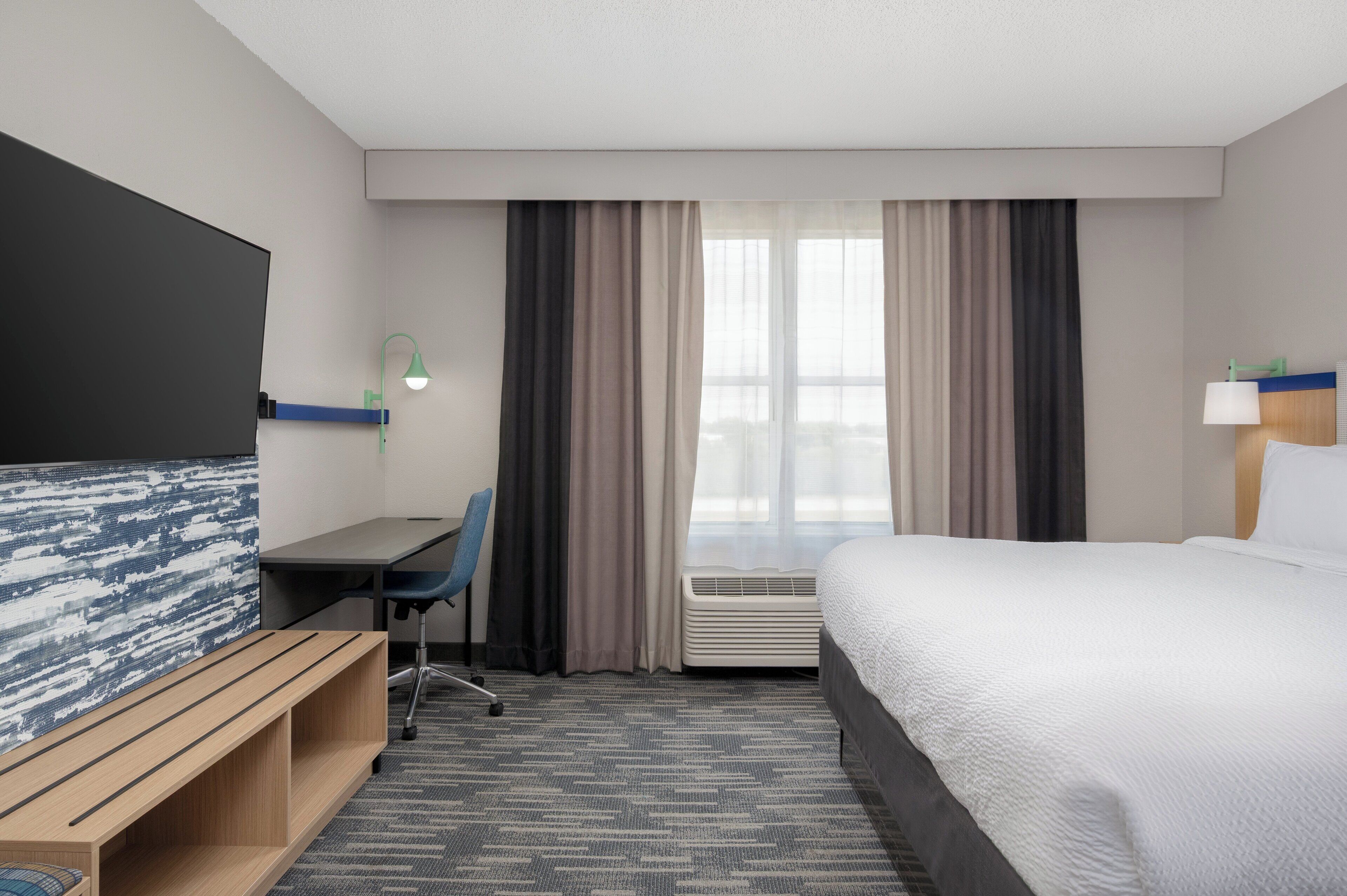 Une chambre d’hôtel équipée d’un lit, d’un bureau, d’une chaise, d’une télévision et d’une fenêtre avec des rideaux.