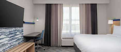 A hotel room with a bed, a desk, a chair, a TV, and a window with curtains.