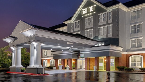 Ein Hotel mit einem gut sichtbaren 'Garner by IHG'-Schild, einem überdachten Eingangsbereich und einer Ziegel-Fassade.