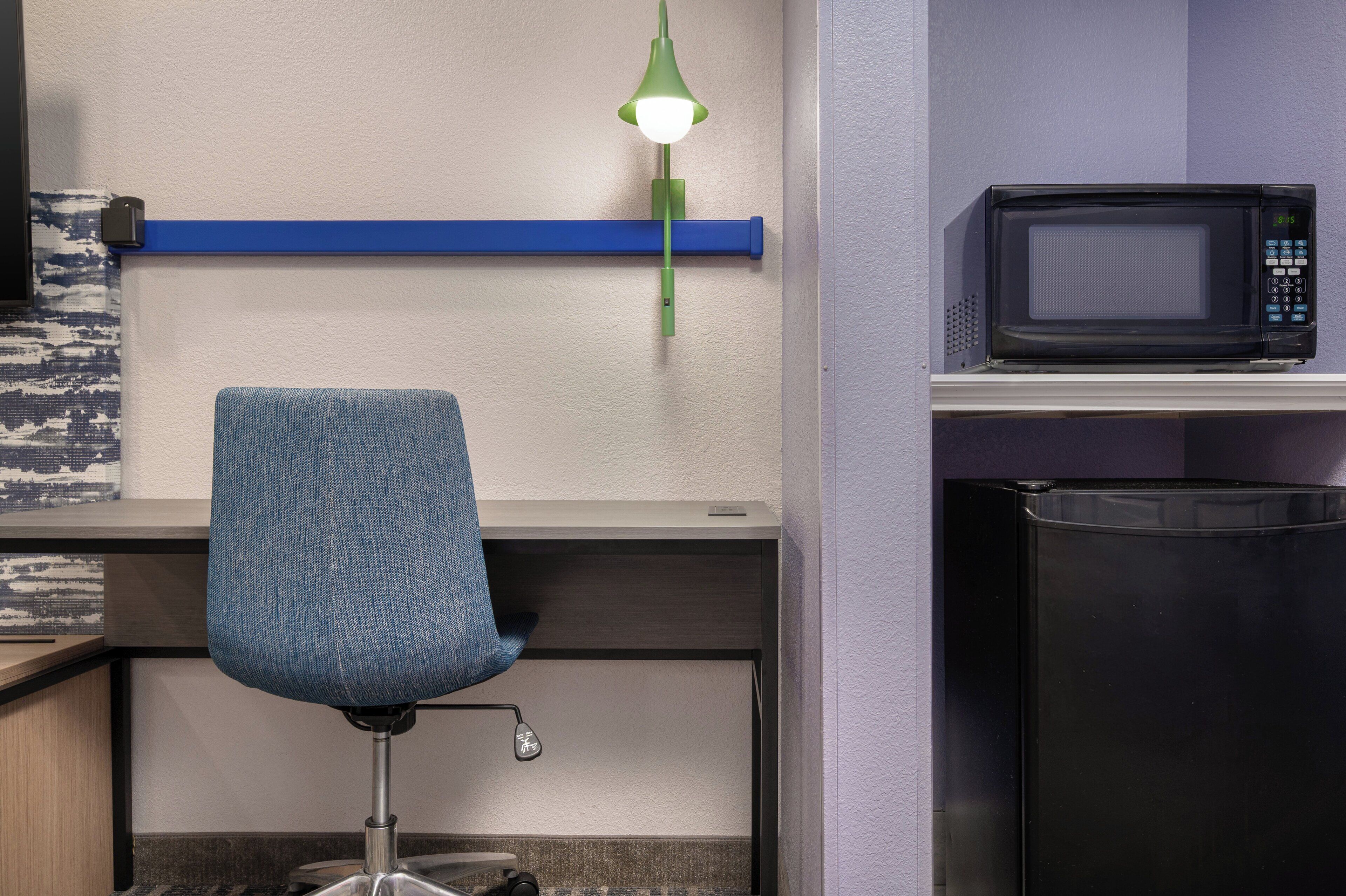 A kitchenette with a microwave, a blue chair, and a green pendant light.