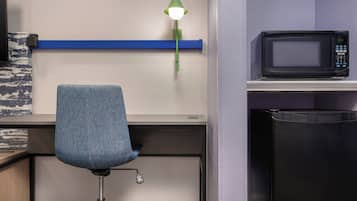 A kitchenette with a microwave, a blue chair, and a green pendant light.