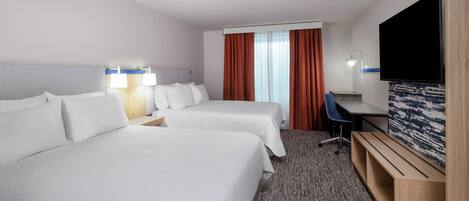 Habitación de hotel con dos camas, un escritorio, un televisor y una ventana con cortinas.
