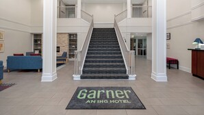 A hotel lobby with a central staircase, a reception desk, and a seating area with blue sofas. - Garner Hotel Evansville East by IHG (Evansville)