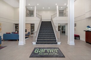 Un vestíbulo de hotel con una escalera central, un mostrador de recepción y una zona de estar con sofás azules.