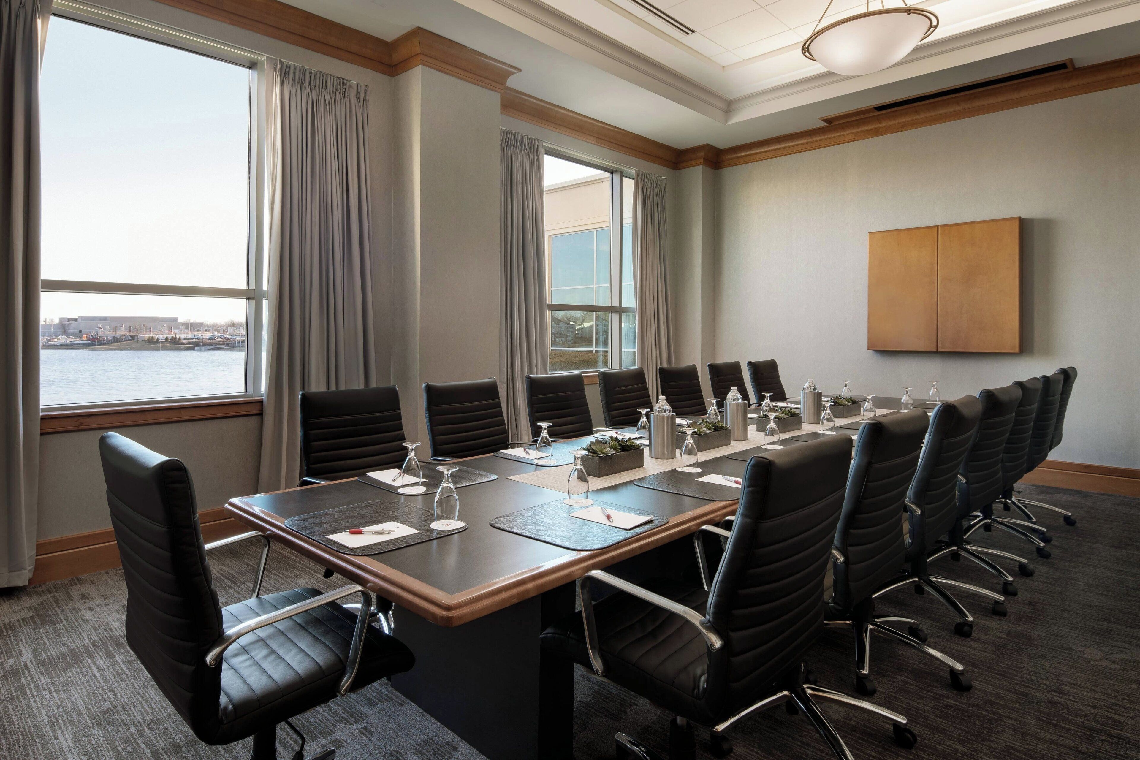 A conference room with a long table, multiple chairs, and a view of a body of water through large windows.