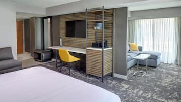 A modern hotel room with a large bed, a desk with a chair, a sofa, and a television mounted on the wall.