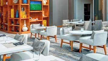 Un moderno vestíbulo de hotel con una gran estantería de madera, zonas de estar cómodas y un televisor mostrando un partido deportivo.