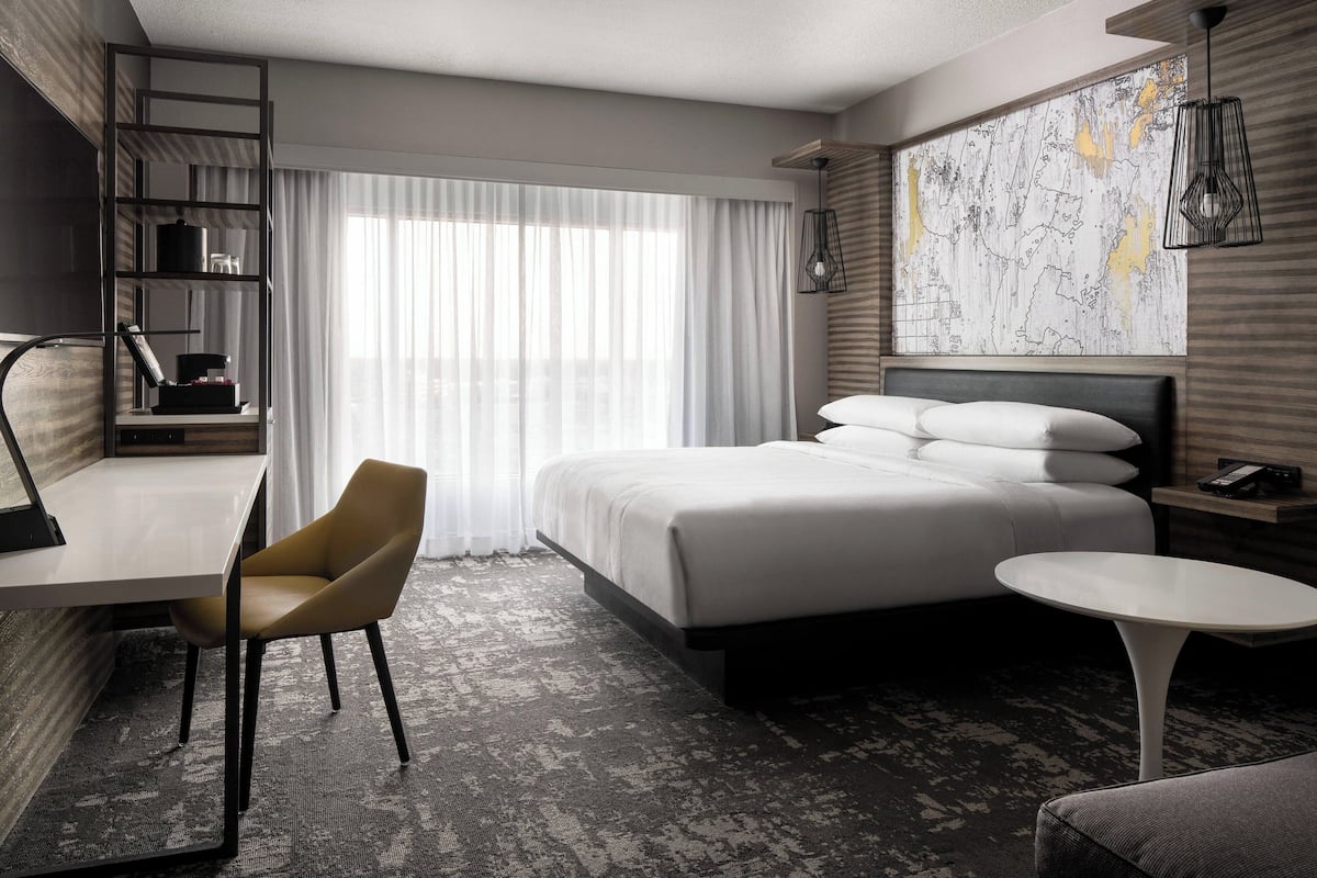 A modern hotel room with a bed, desk, chair, and a small table.