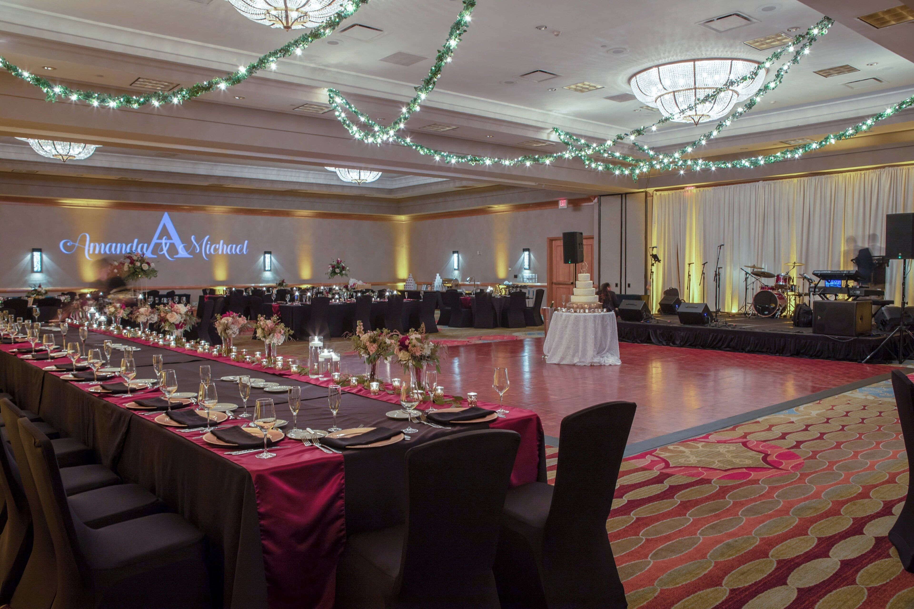 Une salle de banquet avec de longues tables dressées pour un événement formel, une scène avec des instruments de musique et un lustre.