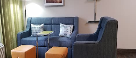 A living room with a blue sofa, two ottomans, a small table, and a lamp.