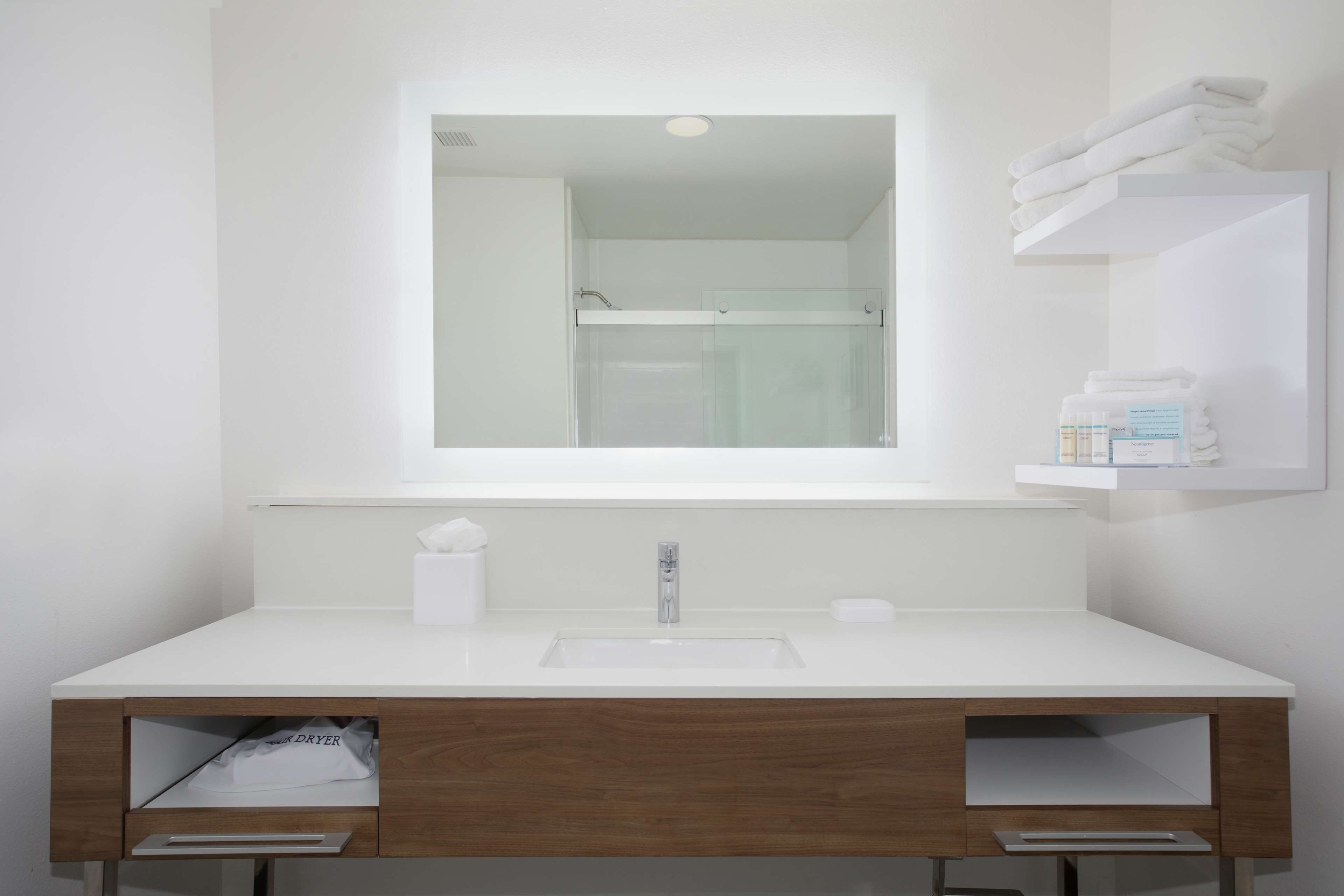 Un baño moderno con tocador blanco, un espejo y un box de ducha de vidrio.