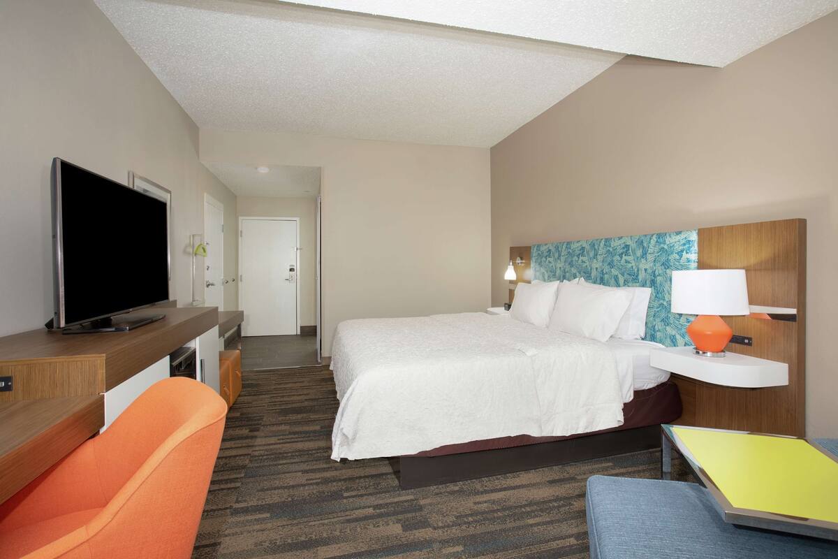 A hotel room with a bed, a TV, a desk, and a chair.