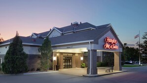 Entrada de un hotel Hampton Inn & Suites bajo un cielo despejado al atardecer.