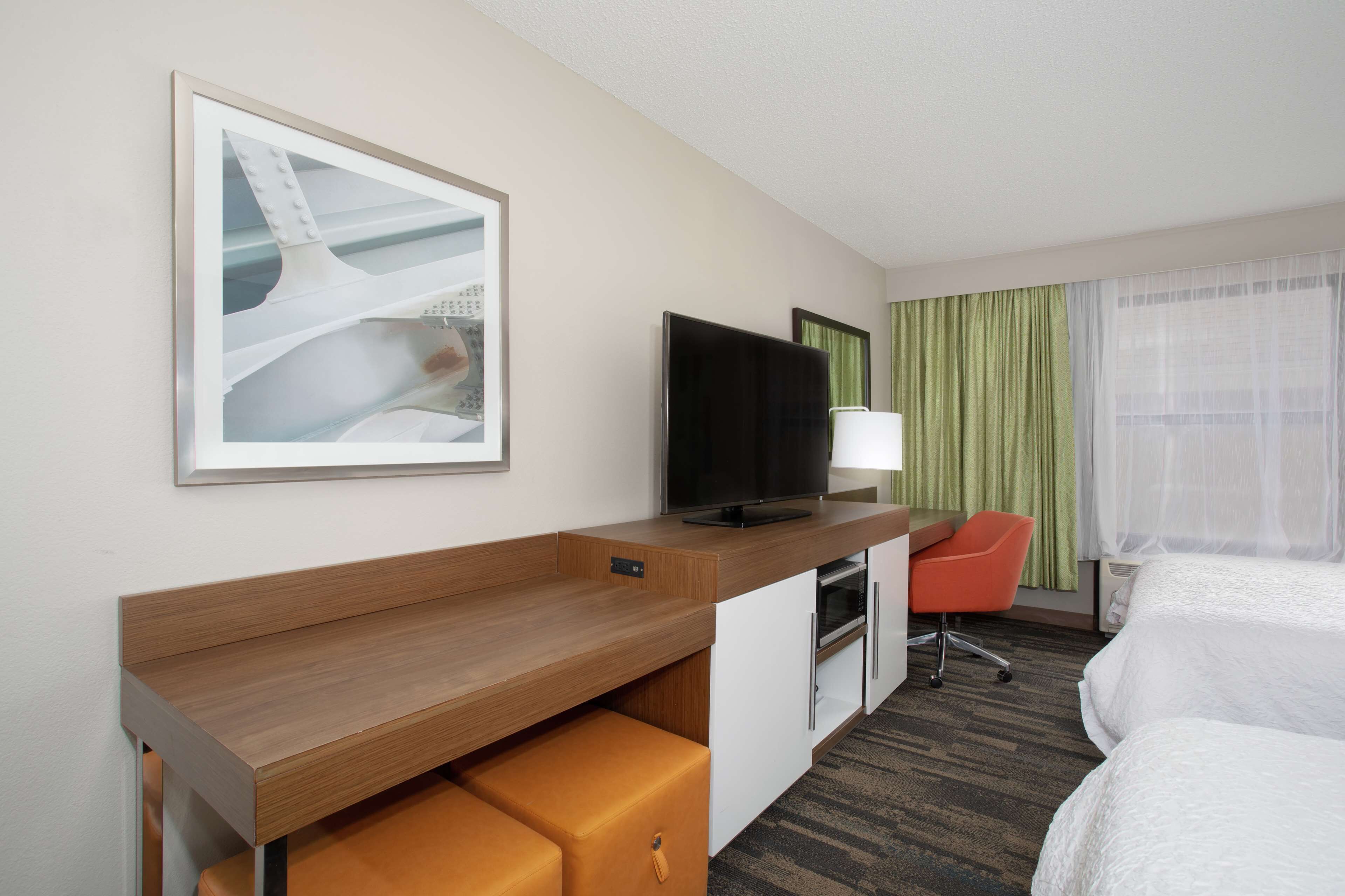 Habitación de hotel con cama, escritorio con silla, televisión y un cuadro en la pared.