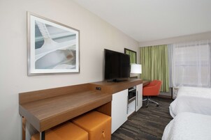 Habitación de hotel con cama, escritorio con silla, televisión y un cuadro en la pared.
