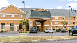 A multi-story hotel with a central entrance, parking lot, and a clear sky. - Quality Inn & Suites University/Airport (Louisville)