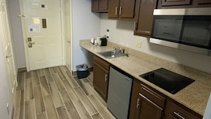 A compact kitchen with wooden cabinets, a stainless steel sink, a dishwasher, and a microwave. - Quality Inn & Suites University/Airport (Louisville)