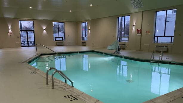 An indoor swimming pool with clear water, surrounded by walls with windows and air conditioning units. - Quality Inn & Suites University/Airport (Louisville)