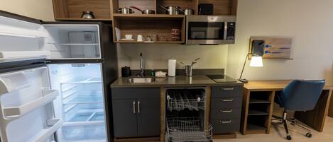 Una cocina compacta con lavavajillas integrado, microondas y una estantería de madera.