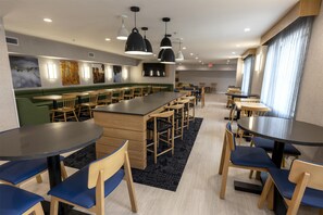 A modern dining area with multiple tables and chairs, a central bar area, and artwork on the walls.