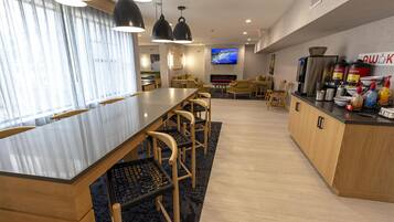 A modern kitchen with a long counter, bar stools, and a TV mounted on the wall.