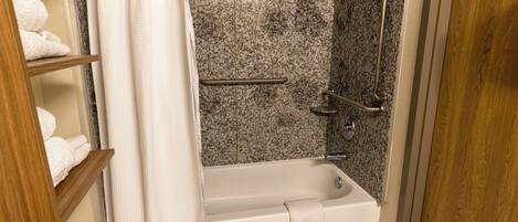A bathroom with a bathtub, a shower with grab bars, and a shelf with towels.