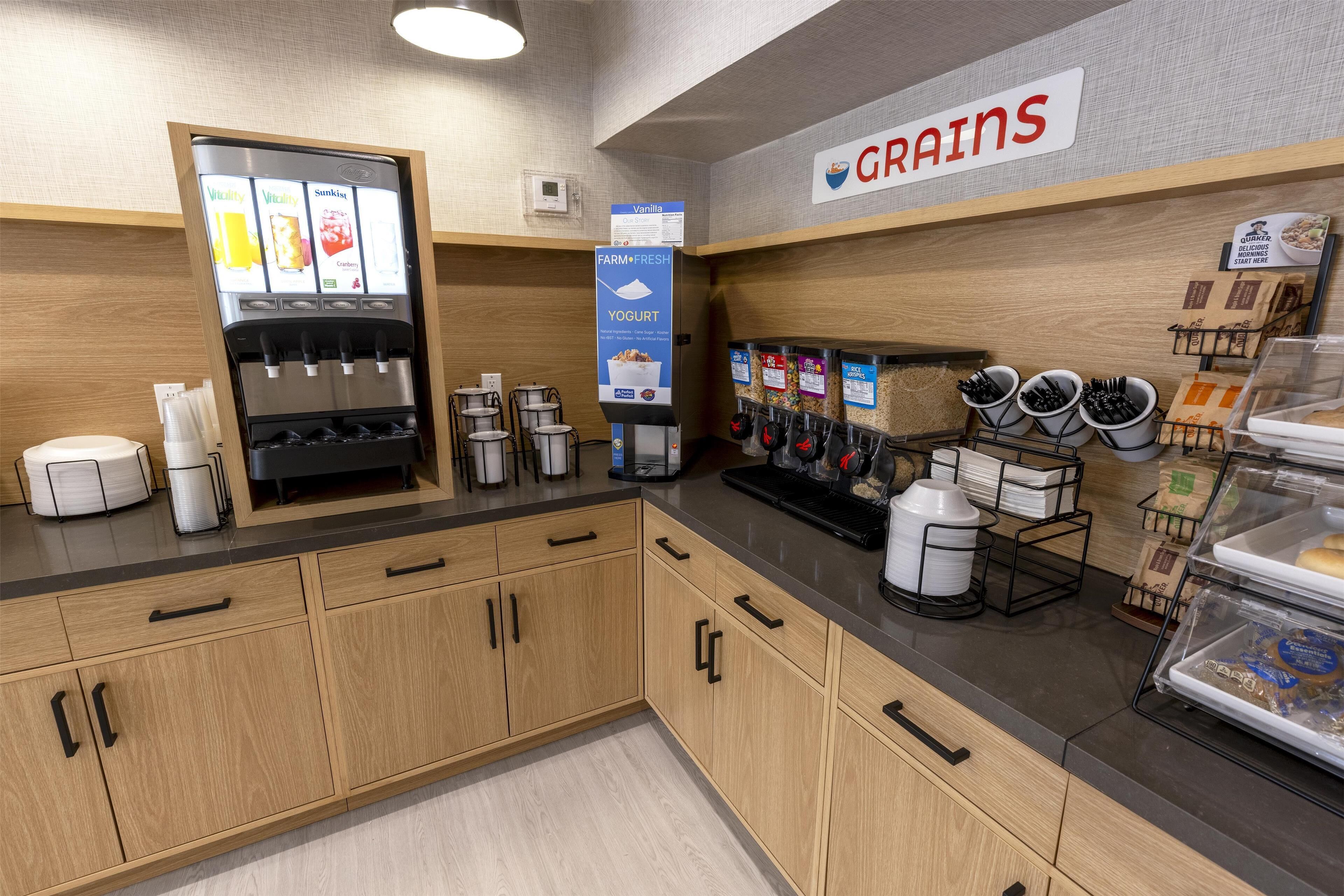 A kitchen area with a yogurt dispenser, coffee machine, and a sign for 'Grains'.