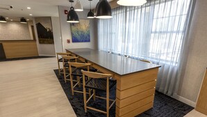 Una habitación de hotel moderna con una barra de madera larga, varios taburetes y un ventanal con cortinas traslúcidas.