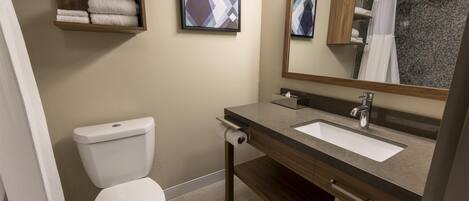 Een badkamer met toilet, wastafel en spiegel. Handdoeken liggen op planken en er is een douchegordijn.