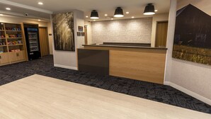 Zona de recepción con un mostrador de madera, una máquina expendedora y una pared con un mural de temática natural.