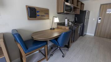 A compact kitchen with a dining table, chairs, a microwave, a refrigerator, and a wooden cabinet.