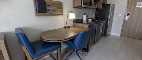 A compact kitchen with a dining table, chairs, a microwave, a refrigerator, and a wooden cabinet.