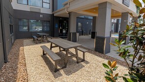 Un espacio al aire libre con mesa de picnic y bancos, rodeado de guijarros y un edificio con el letrero 'Lobby'.