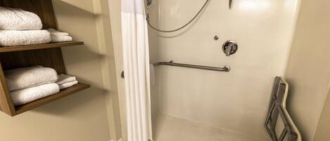 A shower area with a grab bar, a shelf with towels, and a white shower curtain.