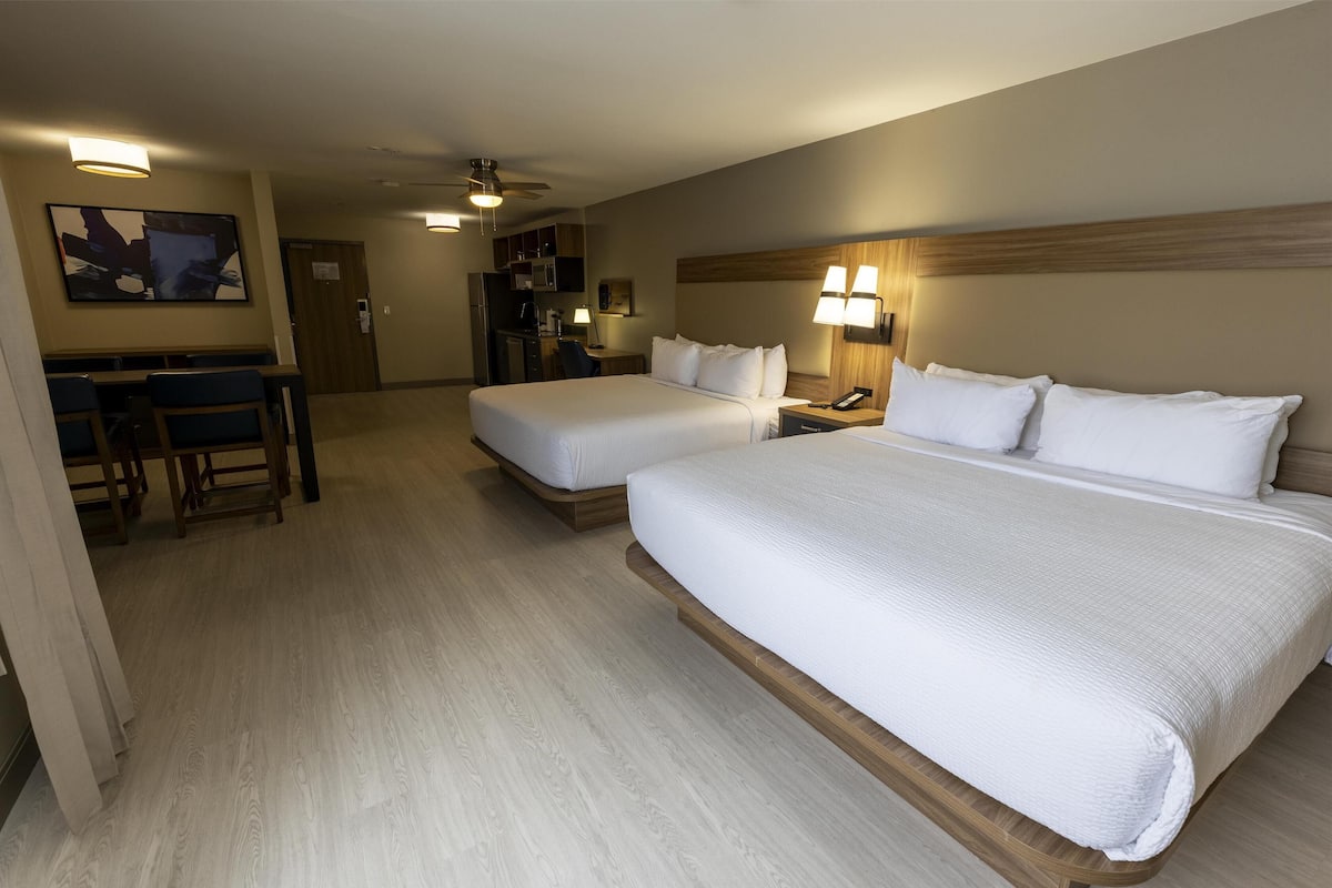 Ein Hotelzimmer mit zwei Betten, einem Schreibtisch, einem Stuhl, einer Schreibtischlampe und einem Deckenventilator.