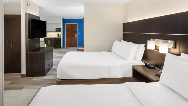 Une chambre d’hôtel avec un lit, une table de chevet, une télévision et, au fond, une petite cuisine.