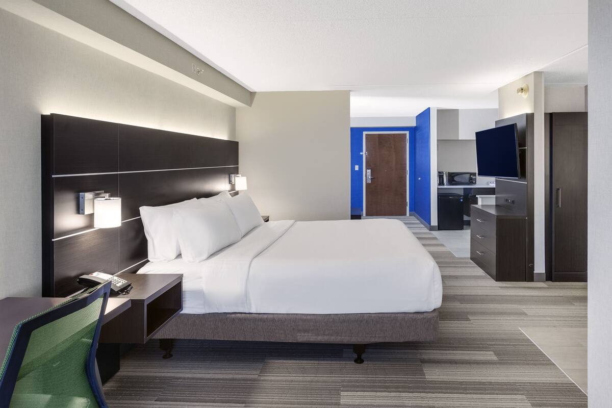 Una habitación de hotel moderna con una cama grande, un escritorio con una silla, una lámpara de escritorio y un televisor de pantalla plana.