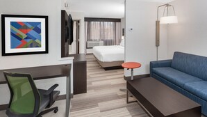 Une chambre d’hôtel avec un lit, un bureau, une chaise, un canapé, une lampe et un tableau encadré au mur.