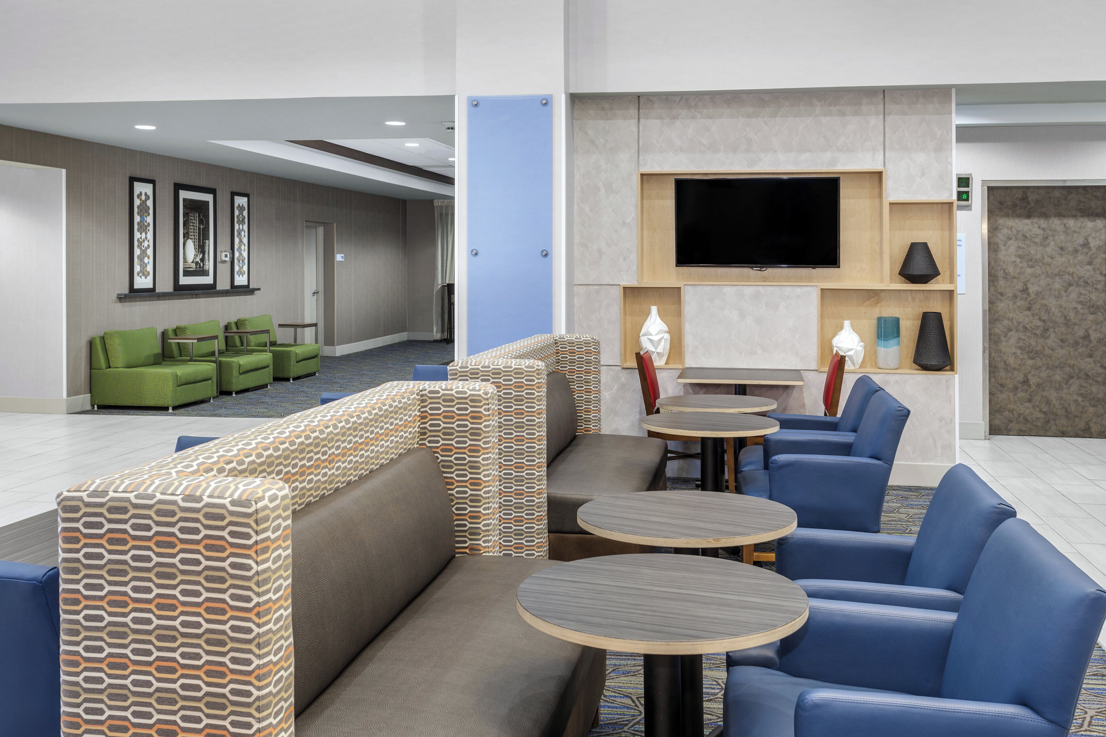 A hotel lobby with seating areas, a flat-screen TV, and a reception desk.