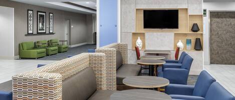A hotel lobby with seating areas, a flat-screen TV, and a reception desk.
