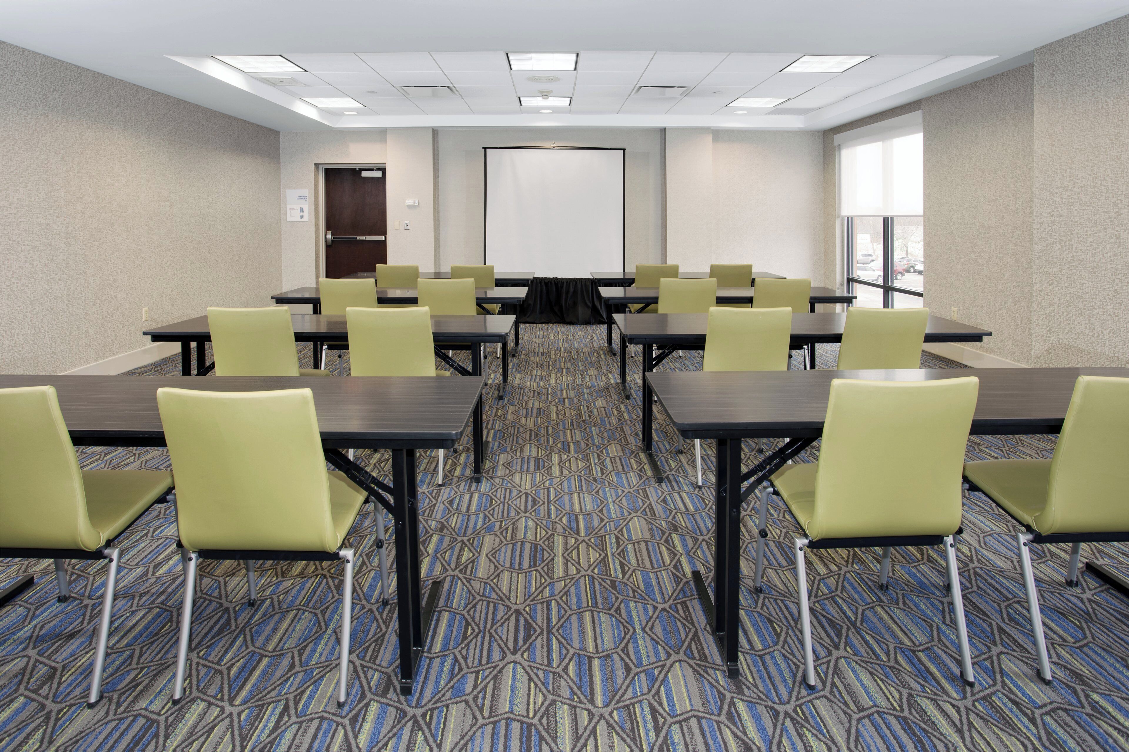 A conference room with tables and chairs, a projector screen, and a patterned carpet.